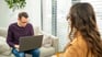 Two people sitting together, one is writing on their laptop